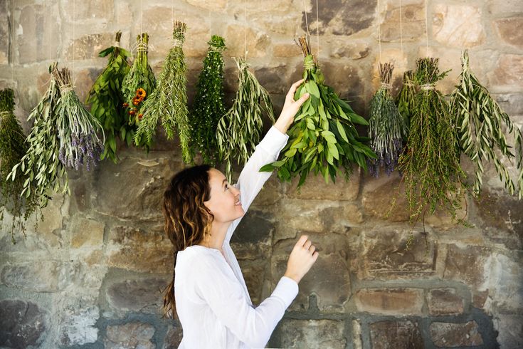 a woman reaching up to plant herbs on a stone wall with greenery hanging from it