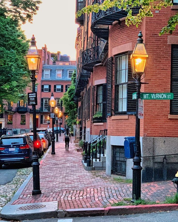 people walking down the street in front of some brick buildings with lights hanging from them