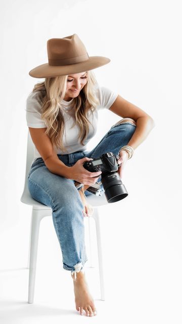 a woman sitting on a chair with a camera in her hand and wearing a hat