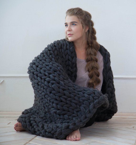 a woman sitting on the floor wrapped up in a gray knitted blanket with braids