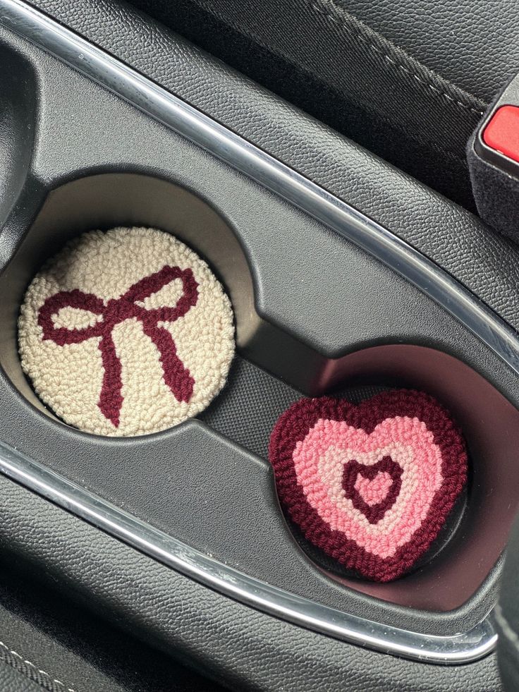 two crocheted heart shaped buttons in the center console of a car, one with a bow on it