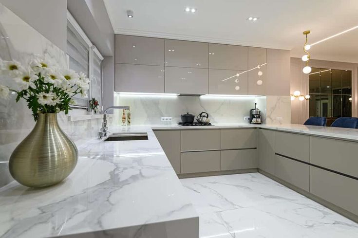 a large kitchen with marble counter tops and white walls, along with gold vases filled with flowers