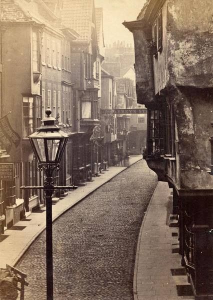 an old photo of a street with buildings on both sides and a lamp post in the middle