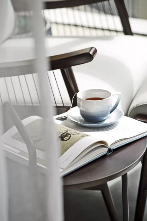 a cup of coffee sitting on top of a table next to a book and chair