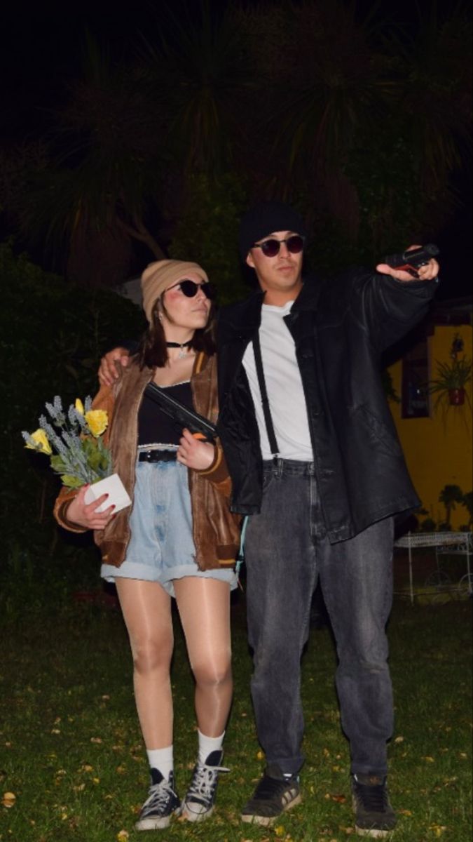 a man and woman standing next to each other in the grass with flowers on their hands