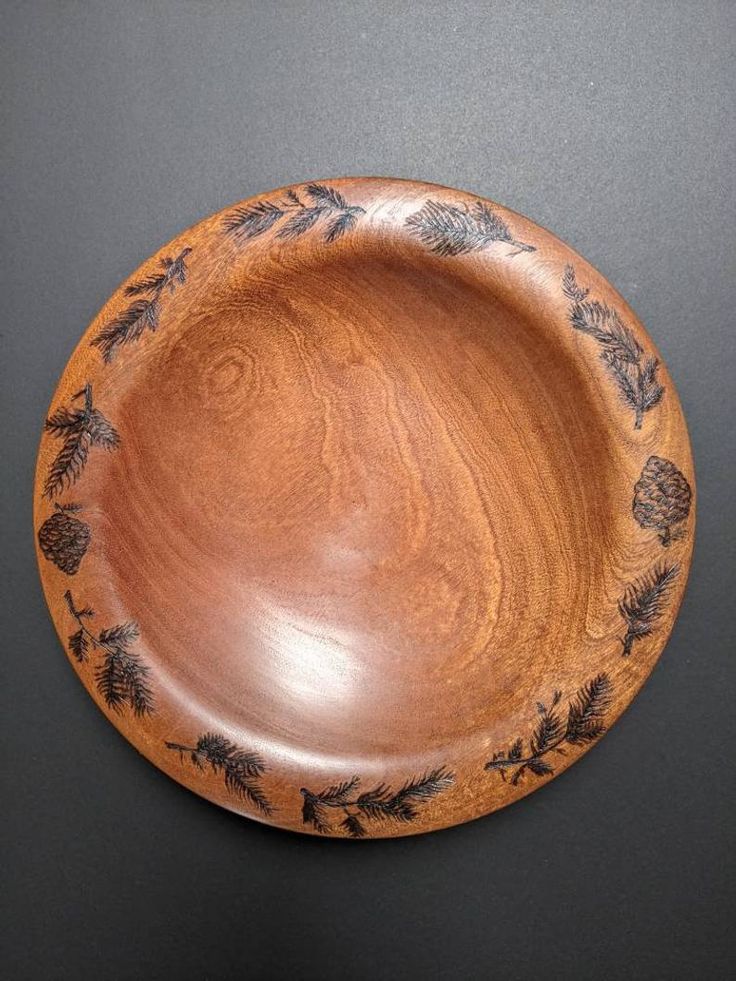 a wooden bowl with pine cones and leaves painted on the side, sitting on a black surface