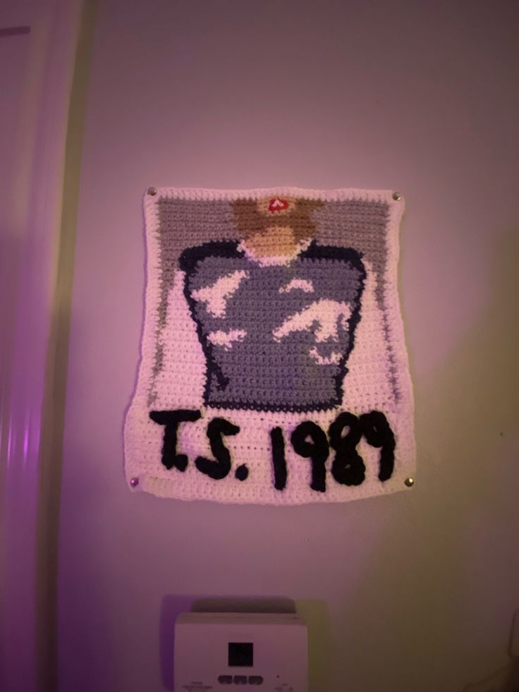 a crocheted photo hanging on the wall in a bathroom with it's name and date