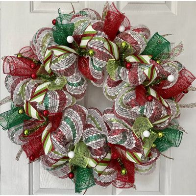 a red and green christmas mesh wreath hanging on a white door with ornaments around it