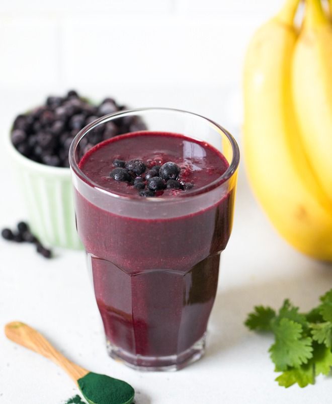 blueberry smoothie in a glass next to bananas