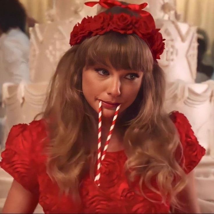 a woman in a red dress drinking from a straw with roses on her head and holding a lollipop