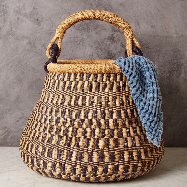 a woven basket with a blue and yellow cloth on it's handle, sitting against a gray wall