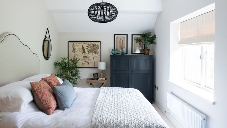 a white bed sitting under a window next to a dresser and windowsill in a bedroom