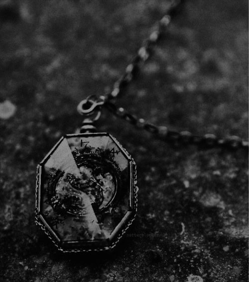 a black and white photo of a necklace on a stone surface, with a chain hanging from it