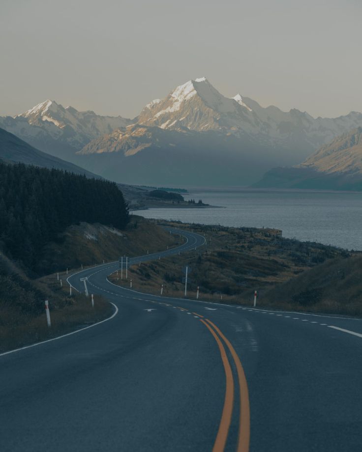 an empty road in the middle of nowhere with mountains in the background and water on either side