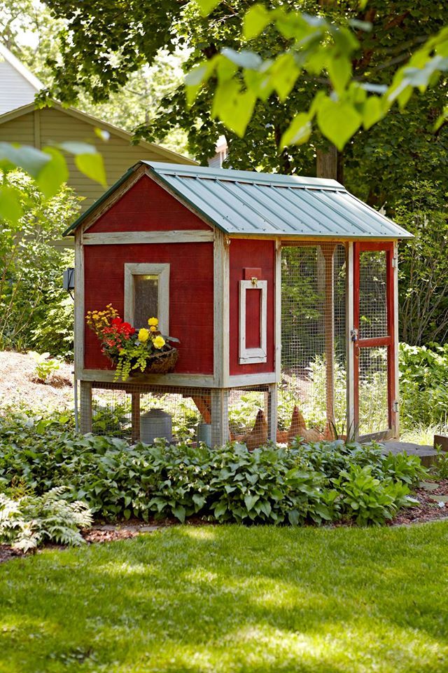 a red chicken coop in the middle of a garden with flowers and plants growing out of it