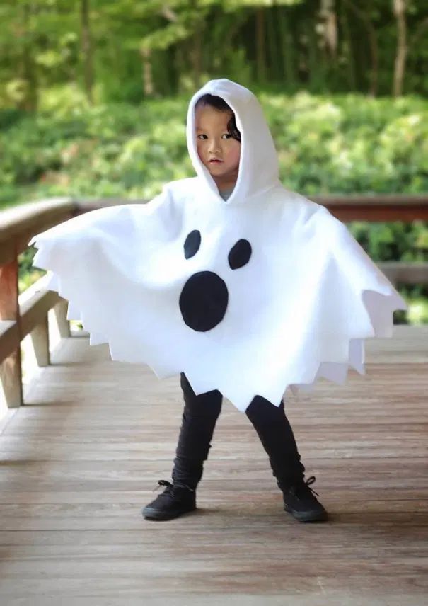 a young boy dressed in a ghost costume standing on a wooden deck with trees in the background