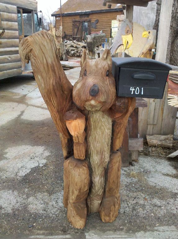 a wooden statue of a squirrel holding a mailbox