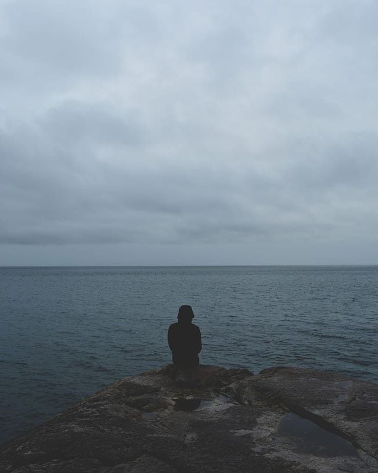 a person sitting on top of a rock near the ocean