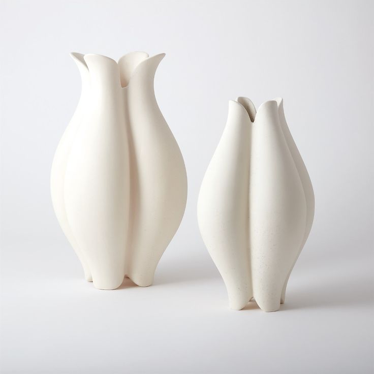 two white vases sitting next to each other on a white surface with no one in it