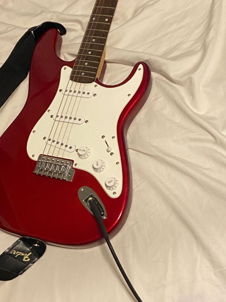 a red electric guitar sitting on top of a bed next to a charger and headphones