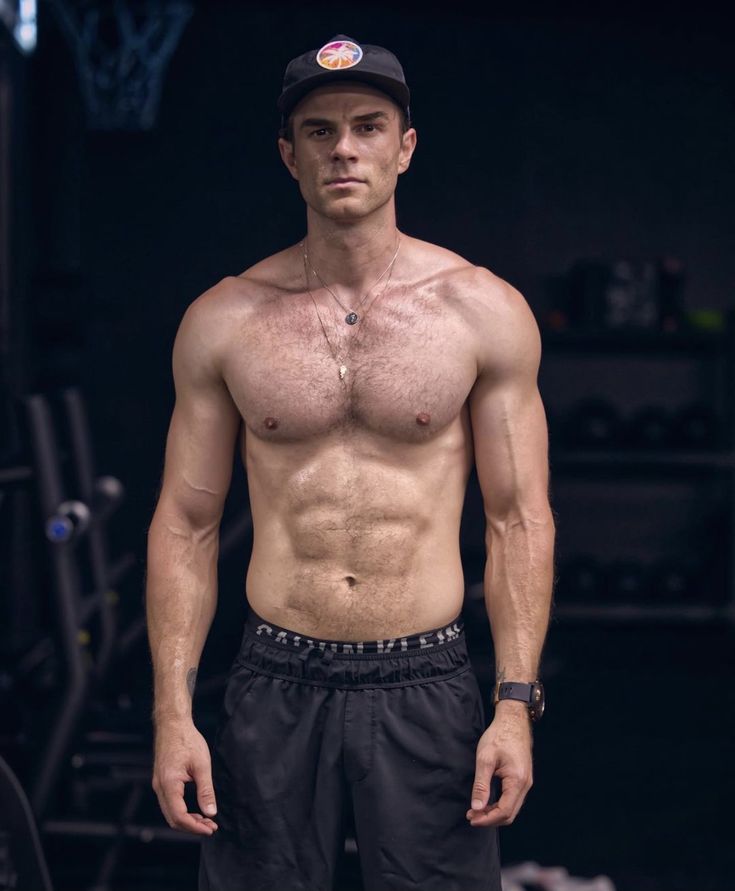 a shirtless man with no shirt standing in front of a gym equipment rack and looking at the camera