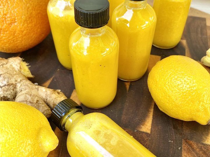 several bottles of yellow liquid sitting on top of a cutting board next to oranges and ginger