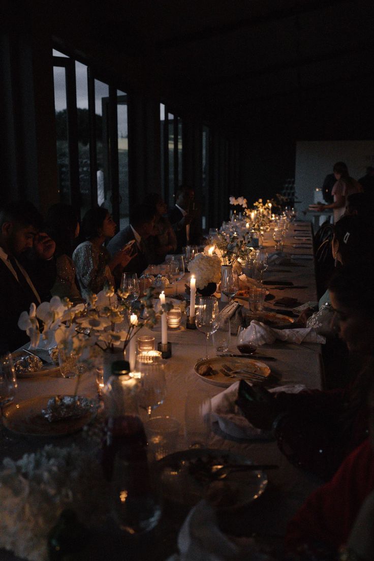 a group of people sitting at a long table with candles in front of their faces