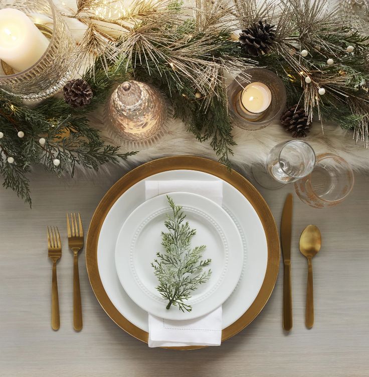 a place setting with pine cones, candles and greenery on the table for christmas dinner