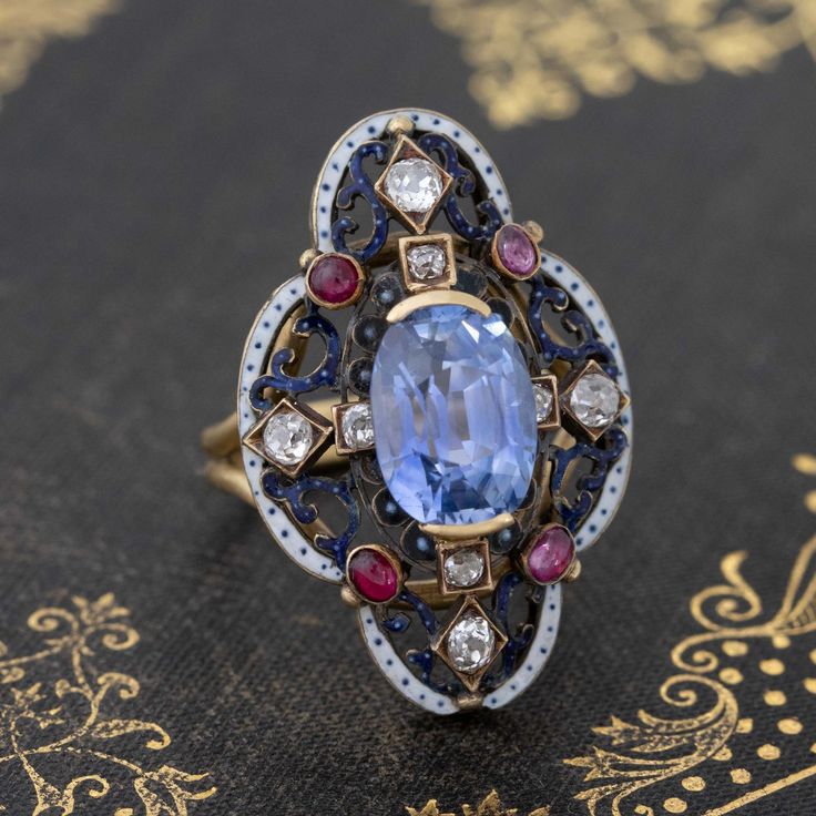 Only one of the prettiest and most special ring we have had the pleasure of owning! The Victorian revival gallery appears to have started its life as a brooch with a shank subsequently added. Really charming details with white enamel and different color gemstones. The sapphire is a stunning medium, almost cornflower blue color - a special no-heat gem! On the finger, it is pretty special. Most def a one of a kind piece. 18kt & 14kt yellow gold Size 6.5 & resizable 4.13ct Sapphire Measures: 10.58 Luxury Sapphire Brooch Jewelry, Victorian Multi-stone White Jewelry, Heirloom Oval Gemstone Brooches, Luxury Enamel Gemstone Ring For Gift, Elegant Multi-stone Oval Brooch, Fine Jewelry Diamond Gemstone Brooches, Luxury Multi-stone Enamel Ring As Gift, Elegant Multi-stone Oval Brooches, Formal White Enamel Gemstone Ring