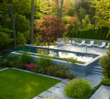 an outdoor swimming pool surrounded by lush green grass and trees with lounge chairs around it