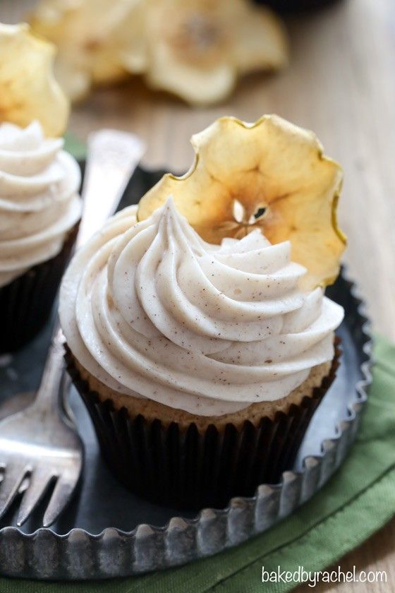 two cupcakes with white frosting and an apple on the top are sitting on a plate