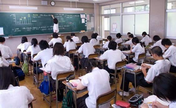 a classroom full of students sitting at desks and writing on the chalkboard in front of them