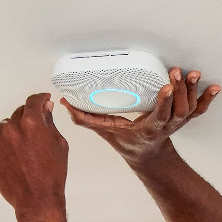 two hands holding an electronic device in the shape of a speaker with blue light on it