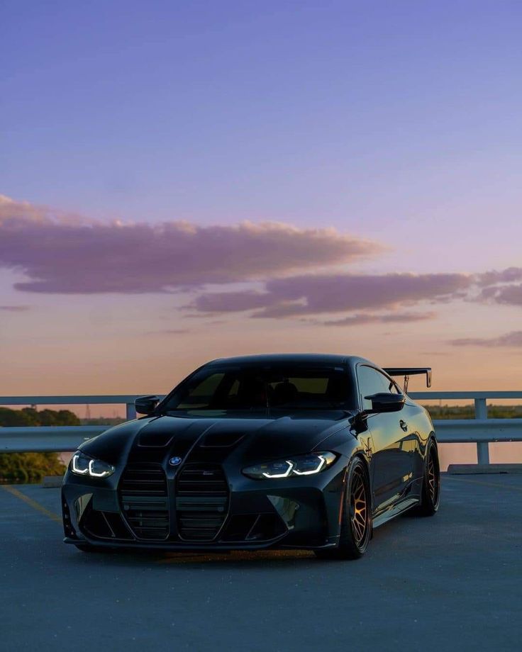 a black sports car parked on the side of a road at sunset or dawn with clouds in the background