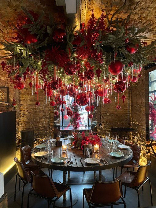 a dining room table decorated with red flowers and greenery hanging from it's ceiling