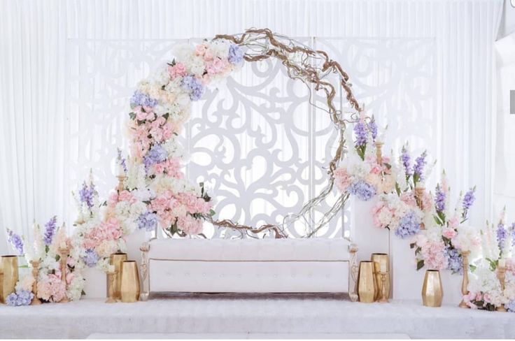 a wedding ceremony with flowers and gold vases on the side of the aisle, in front of a white backdrop