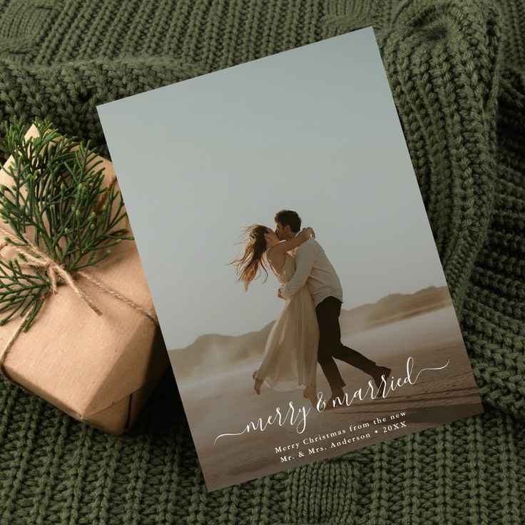 a christmas card with an image of a couple hugging on the beach next to a wrapped present