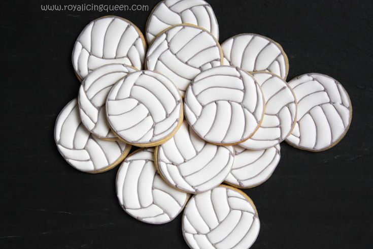 cookies decorated with white icing are arranged in the shape of volleyball balls on a black surface