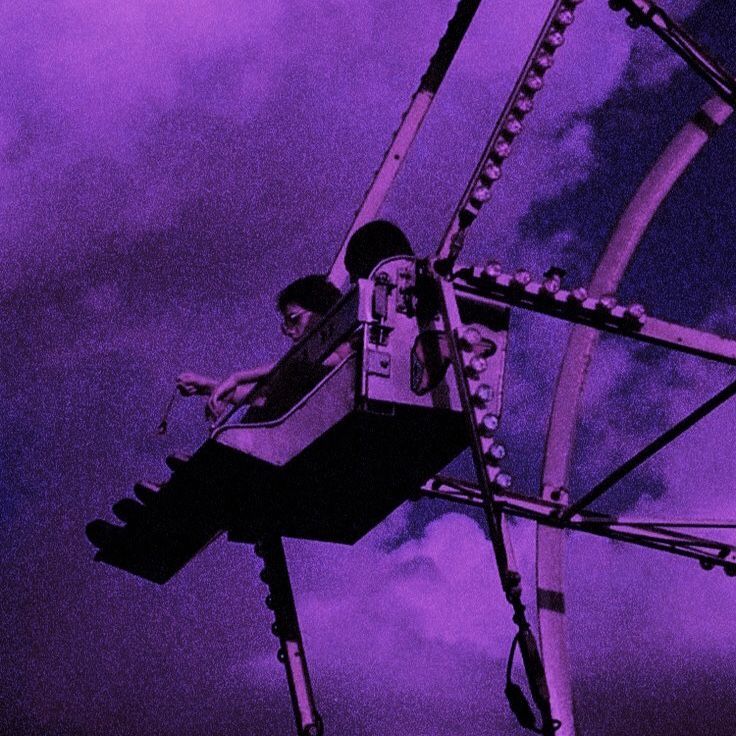 a man riding on top of a ferris wheel under a purple sky filled with clouds