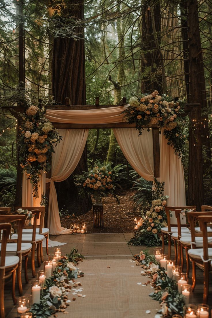 an outdoor ceremony setup with candles and flowers on the aisle, surrounded by tall trees