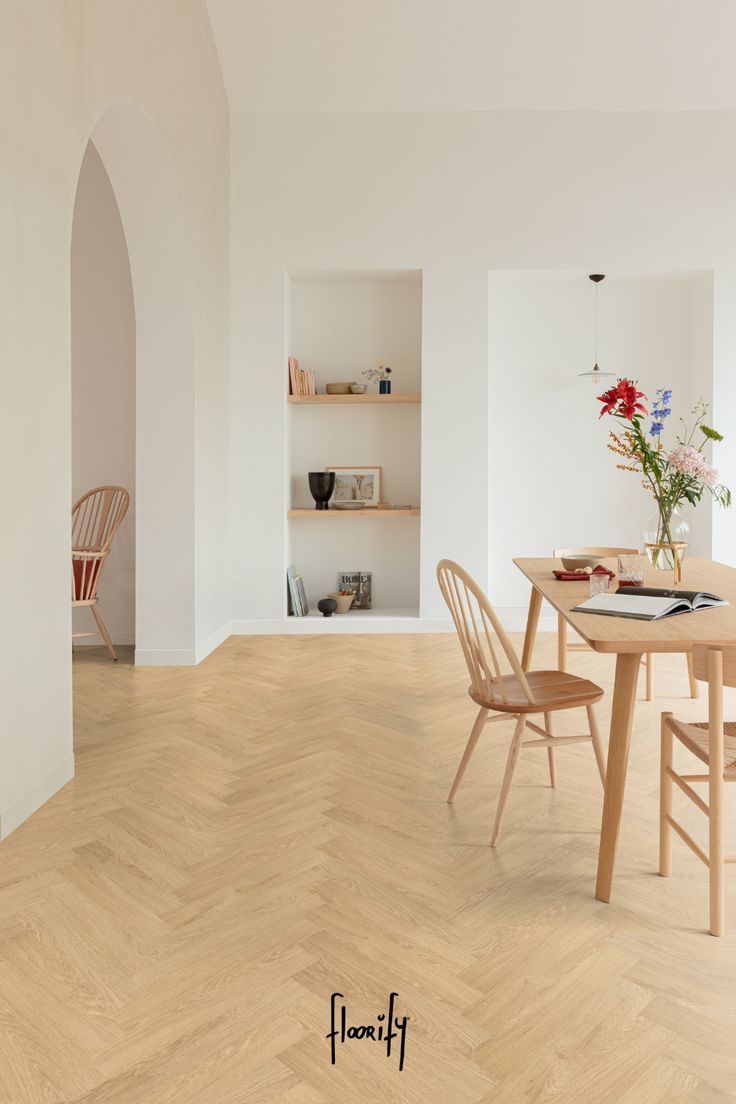 a dining room table with chairs and a vase on top of it in front of a white wall