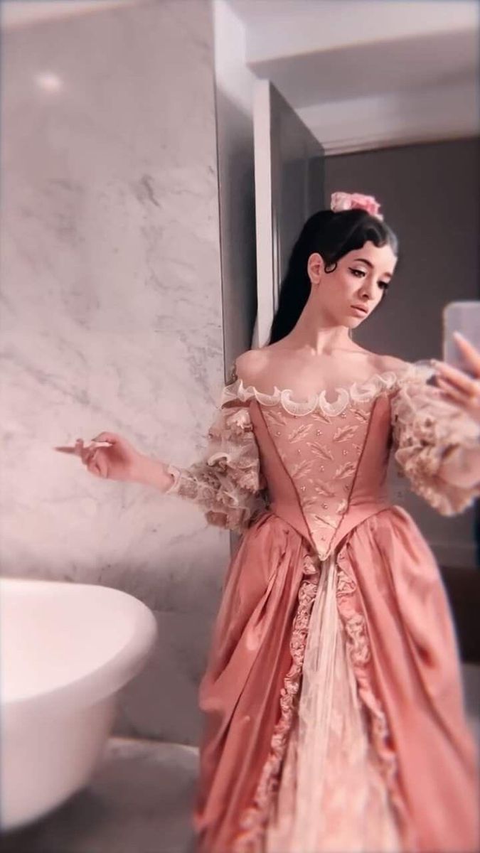 a woman in a pink dress taking a selfie with her cell phone while standing next to a sink