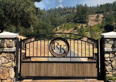 the entrance to an estate with stone and iron gates, surrounded by hills and trees