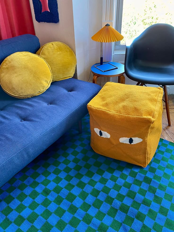 a living room with a blue couch and yellow pillow on the floor next to a black chair