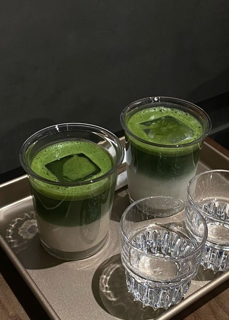 three cups filled with green liquid sitting on top of a metal tray next to each other