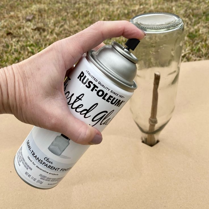 a hand holding a spray paint can next to a broken glass vase on the ground