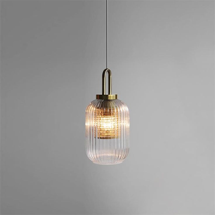 a glass and brass pendant light hanging from a ceiling fixture in an empty room with grey walls