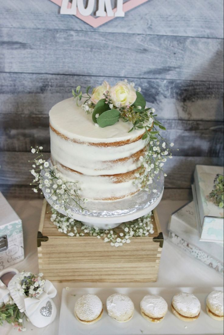 a white cake with flowers and greenery sits on a wooden stand next to other desserts