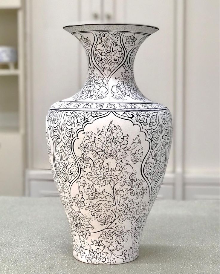 a white and black vase sitting on top of a table next to a bookcase