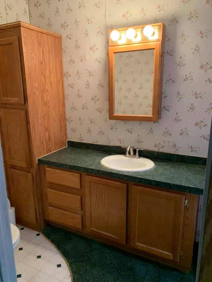 a bathroom with wooden cabinets and green counter tops, along with floral wallpaper on the walls